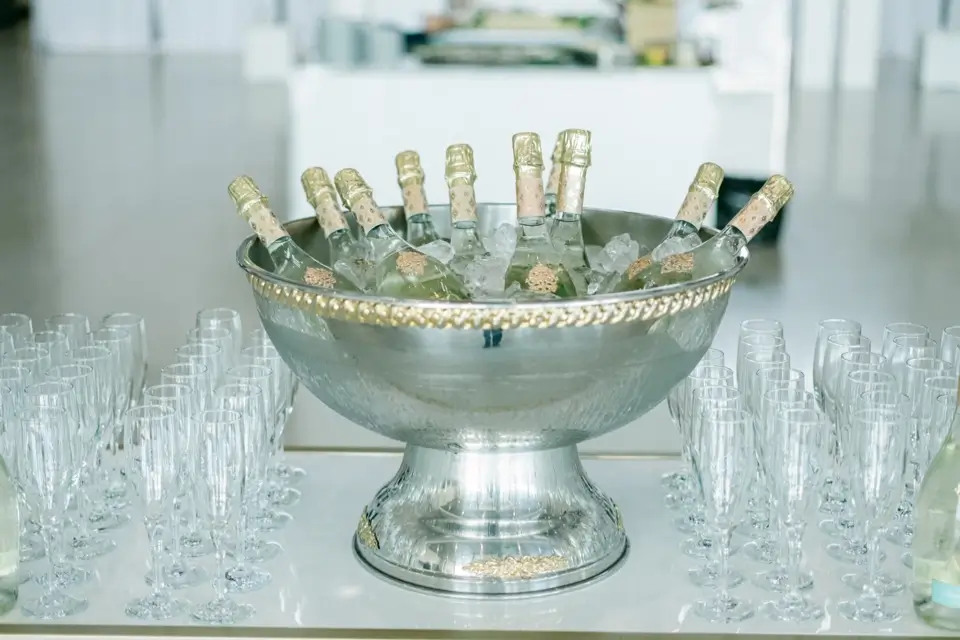 A large silver bowl filled with ice holds several champagne bottles, surrounded by neatly arranged empty champagne flutes on a polished white table. The background is softly blurred, suggesting a formal event setting. 124 on Queen Hotel and Spa | Hotel & Spa Niagara-on-the-lake | 1 (855) 988-4552