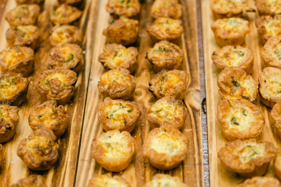 Rows of small, golden-brown pastry puffs filled with a creamy mixture are placed on wooden boards. The pastries are evenly spaced and appear freshly baked, with slightly crispy and flaky edges. 124 on Queen Hotel and Spa | Hotel & Spa Niagara-on-the-lake | 1 (855) 988-4552