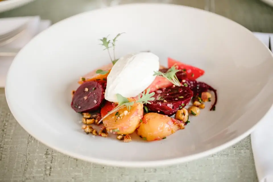 A white plate featuring a vibrant salad with sliced beets, orange segments, nuts, and a dollop of creamy white cheese or yogurt on top. The dish is garnished with small green herbs. 124 on Queen Hotel and Spa | Hotel & Spa Niagara-on-the-lake | 1 (855) 988-4552