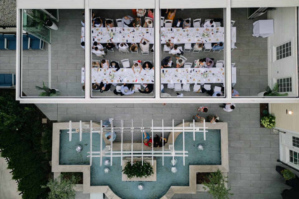 Aerial view of two long dinner tables filled with guests in an outdoor patio area, next to a geometric fountain with flowing water and greenery. 124 on Queen Hotel and Spa | Hotel & Spa Niagara-on-the-lake | 1 (855) 988-4552